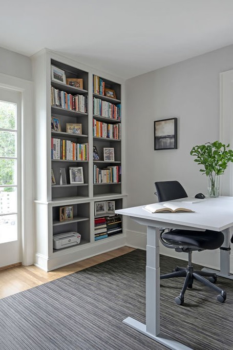 Minimalist, contemporary and urban penthouse interior home office design by Orlie Katsiris Staging & Interiors featuring modern furniture, a black standing desk, white ergonomic chair, and a gray geometric area rug